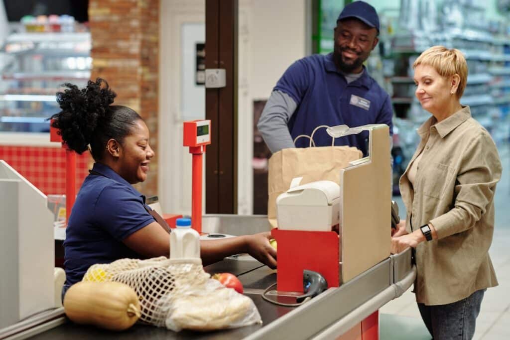 Happy young female cashier scanning food products chosen by customer